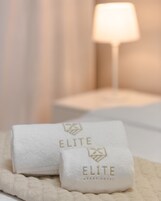 Dos toallas blancas con el bordado 'ELITE', sobre una cama con cubrecolchón acolchado.