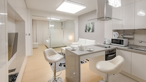 A modern kitchen with white cabinetry, a central island with seating, a microwave, and a sink.