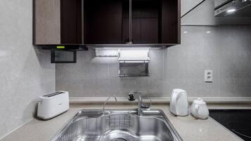 Una cocina moderna con un lavamanos de acero inoxidable, un tostador empotrado y una tetera.