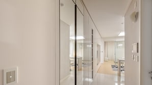 A modern hotel corridor with glass partitions, a clean tiled floor, and a visible bathroom area with a sink and toilet.