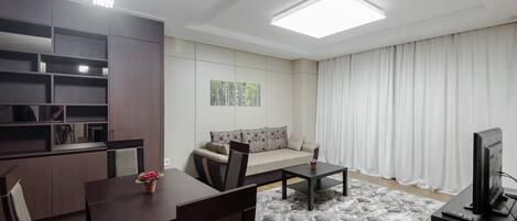 A modern living room with a sofa, dining table, chairs, a TV, and a ceiling light.