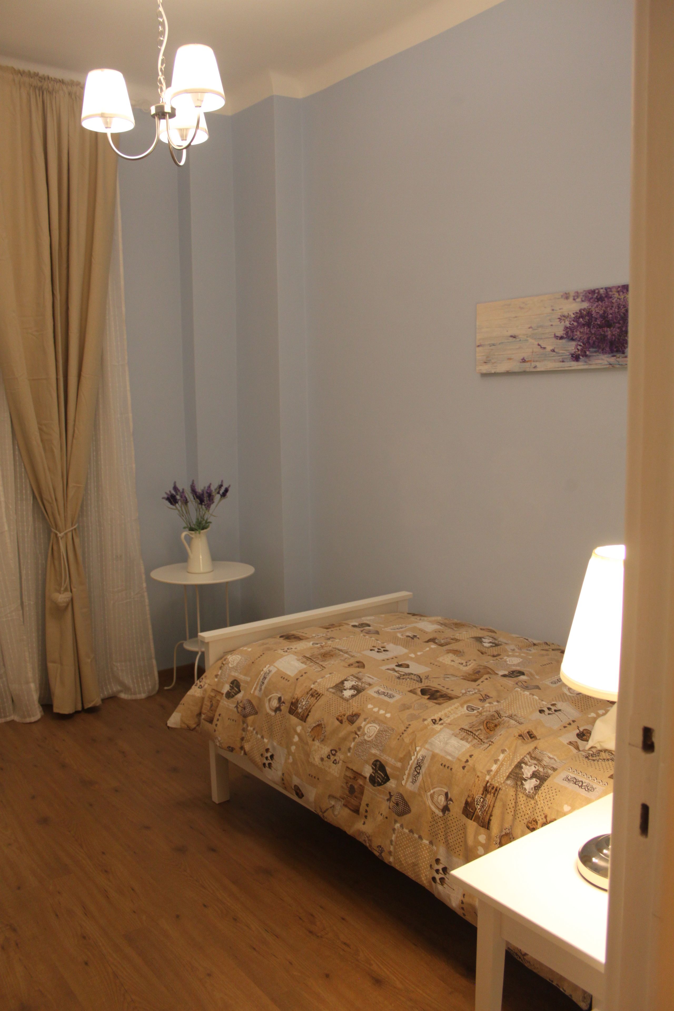 A bedroom with a bed, a bedside table, a lamp, a small table with a vase of flowers, and a painting on the wall.