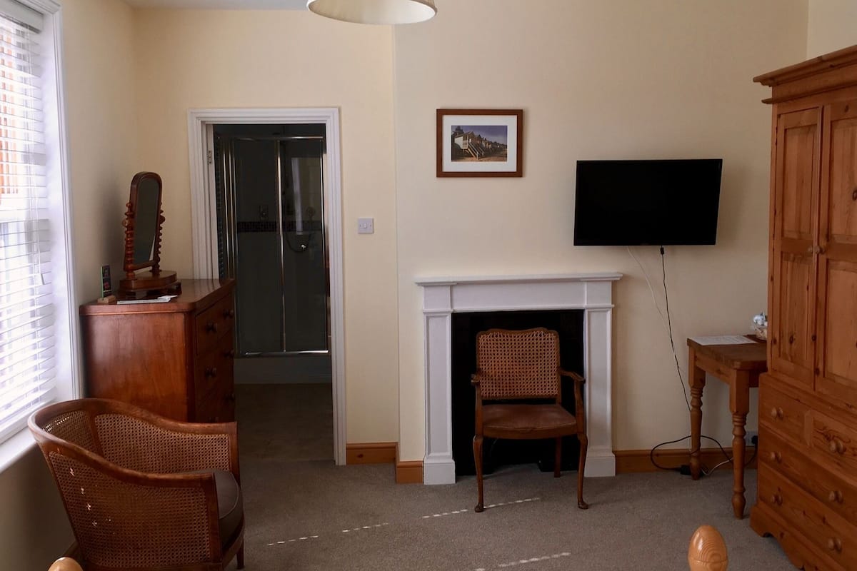 A living room with a fireplace, a television mounted on the wall, a wooden cabinet, and a wicker chair.