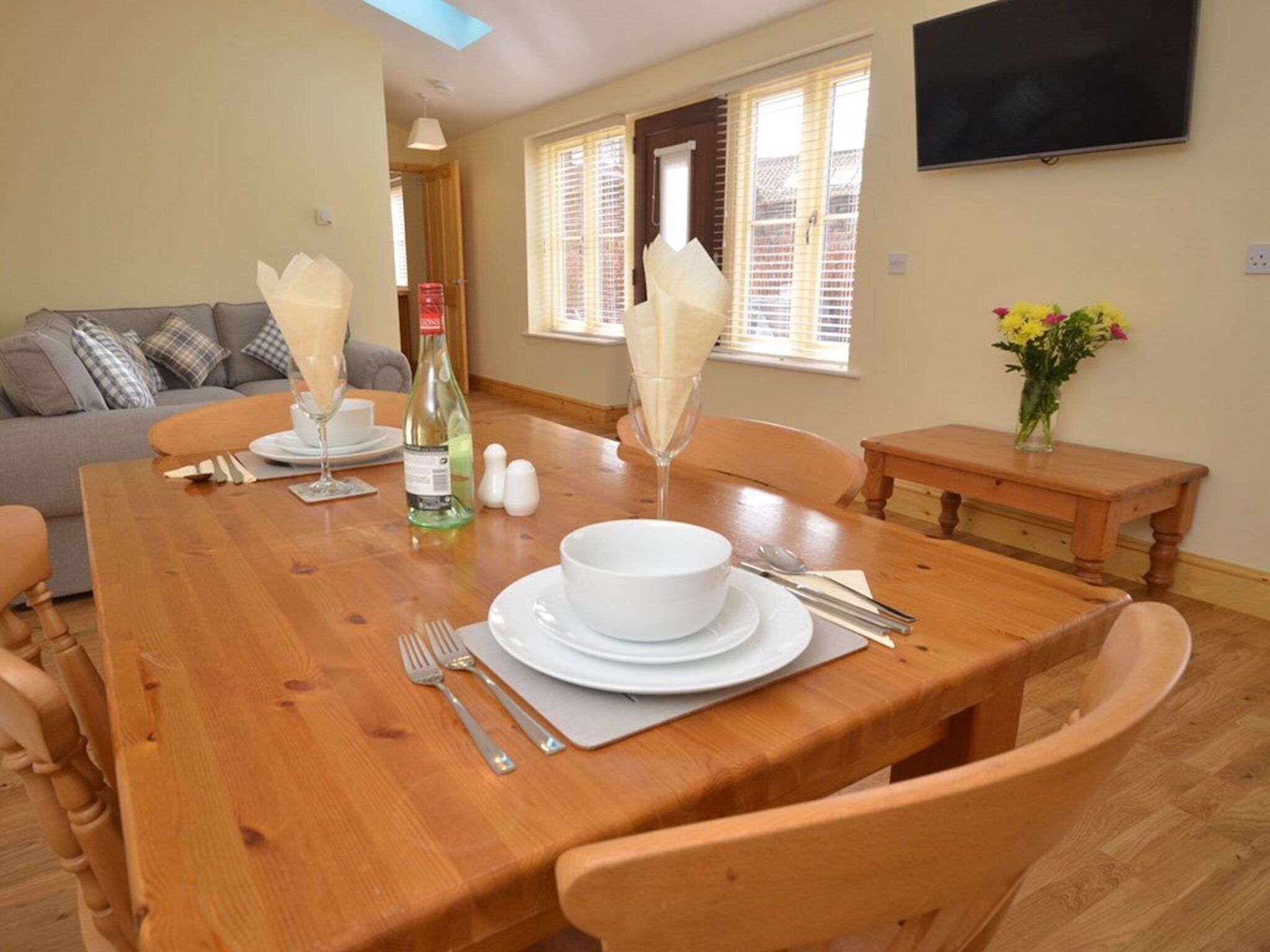 Un coin repas avec une table en bois mise pour quatre personnes, comprenant des assiettes, des couverts et une bouteille.