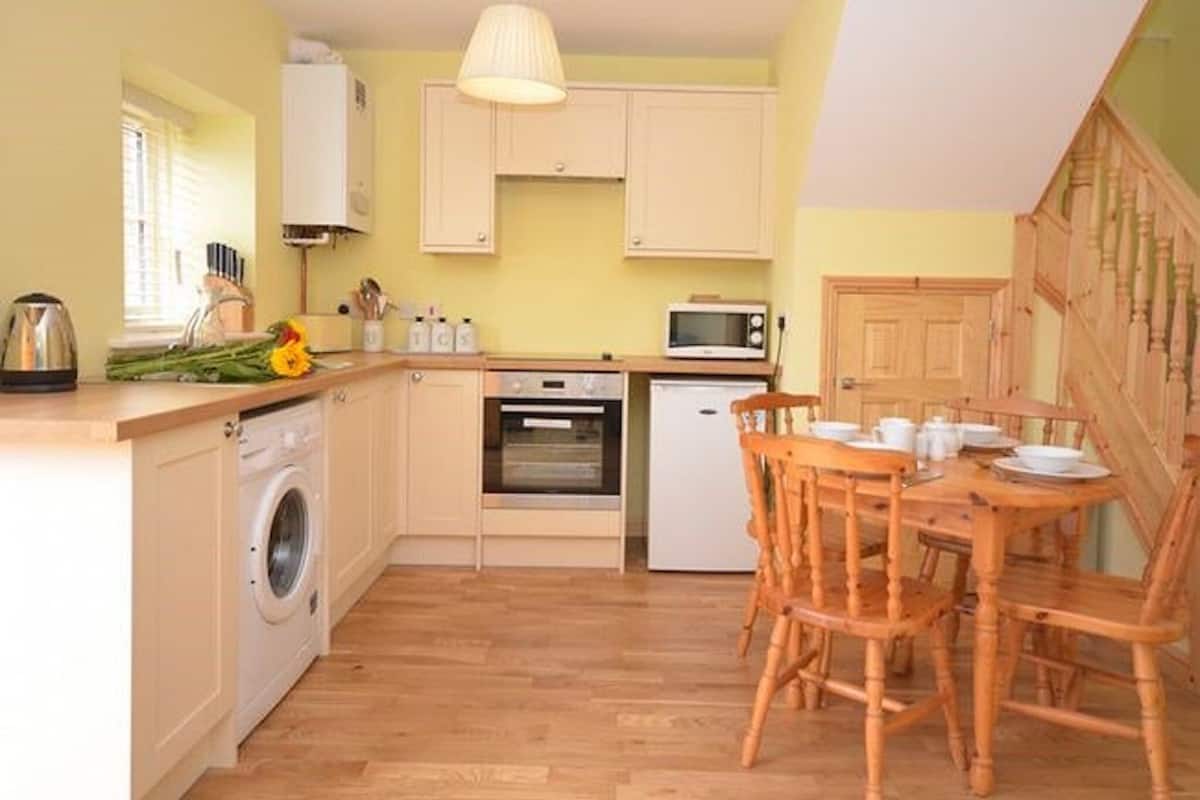A compact kitchen with a washing machine, oven, microwave, and wooden dining table with chairs.