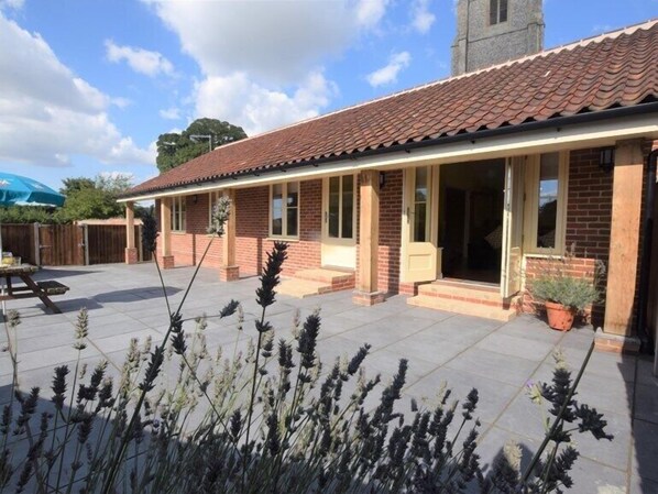 A two-story brick house with a tiled roof, a covered patio, and a small garden with lavender plants. - The White Lady (North Walsham)