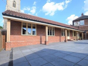 A two-story building with a tiled roof, a brick facade, and a large open patio area. - The White Lady (North Walsham)