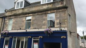 A two-story building with a 'TO LET' sign, a blue facade, and a flower box on the ground floor. - 1 Varis Apartments (Forres)