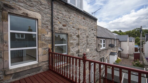 A stone building with a wooden deck and a red railing. - 1 Varis Apartments (Forres)
