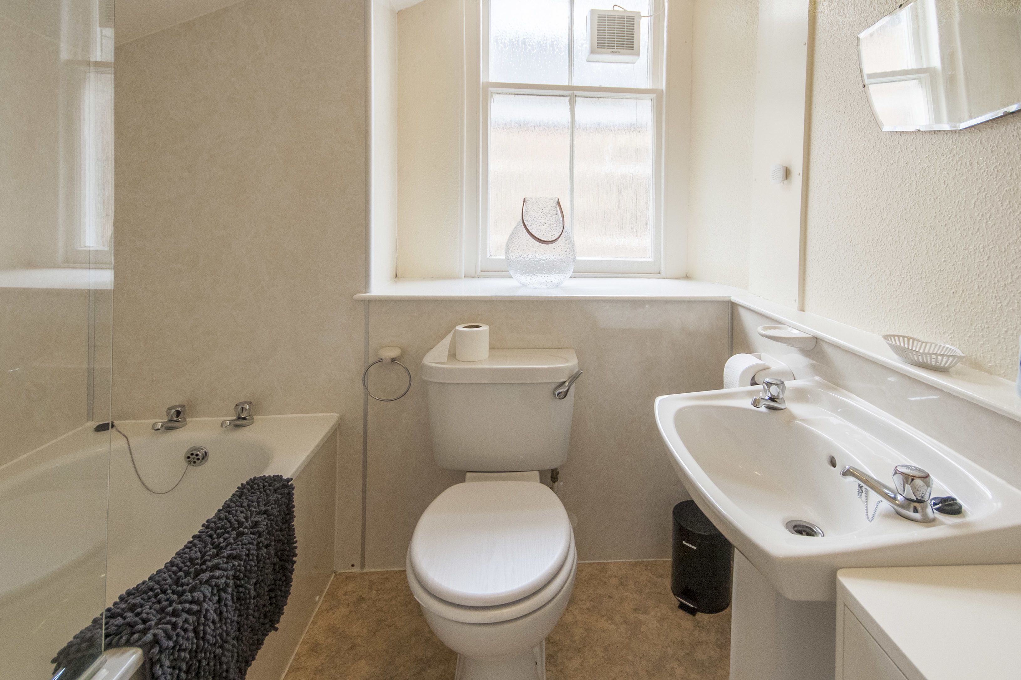 A bathroom with a bathtub, toilet, sink, and a window with a vase.