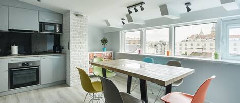 Cocina moderna con armarios grises, microondas y horno. Cuenta con un comedor con mesa de madera y sillas coloridas.