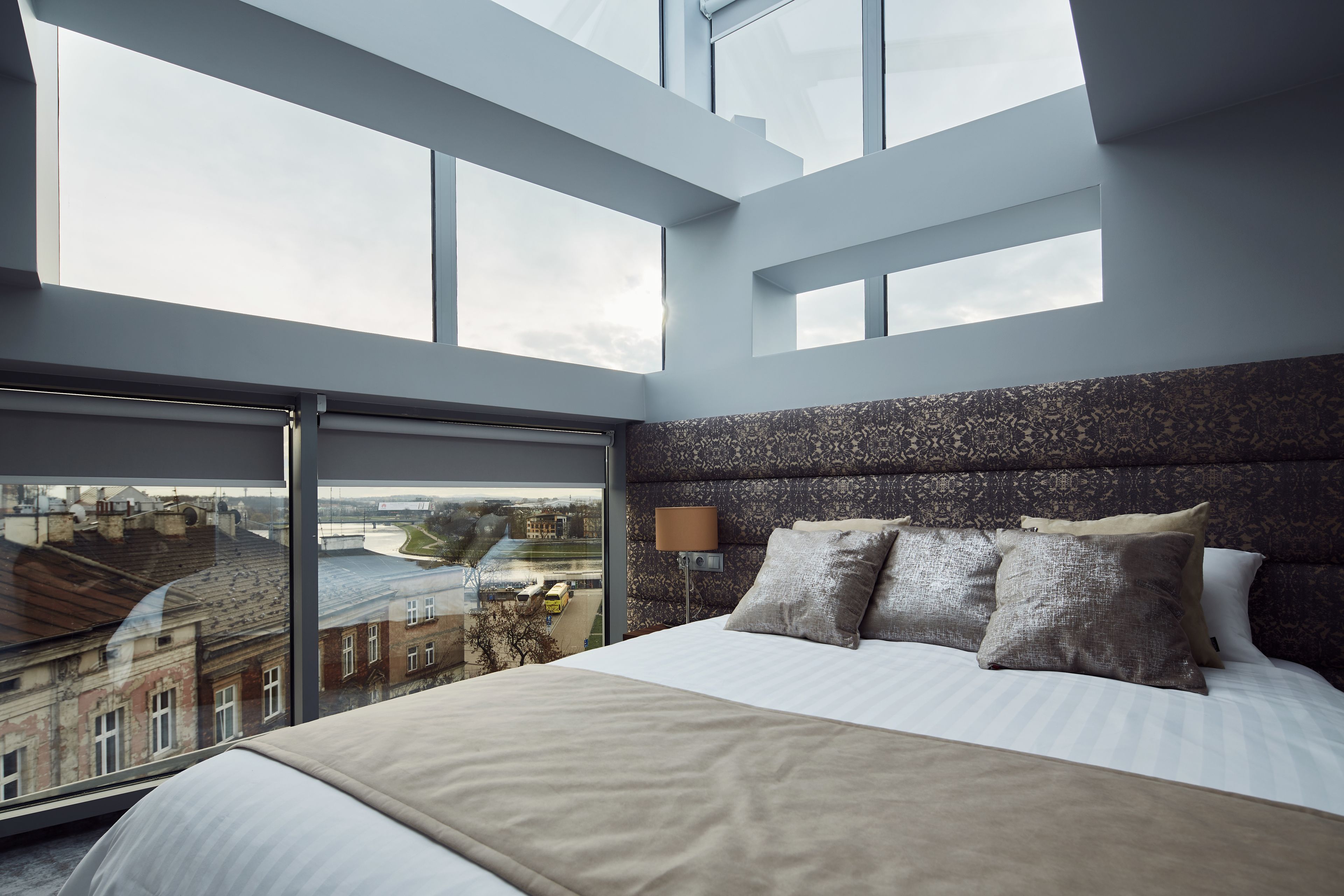 Un dormitorio moderno con una cama grande, cabecera con textura y vista a la ciudad a través de ventanales.