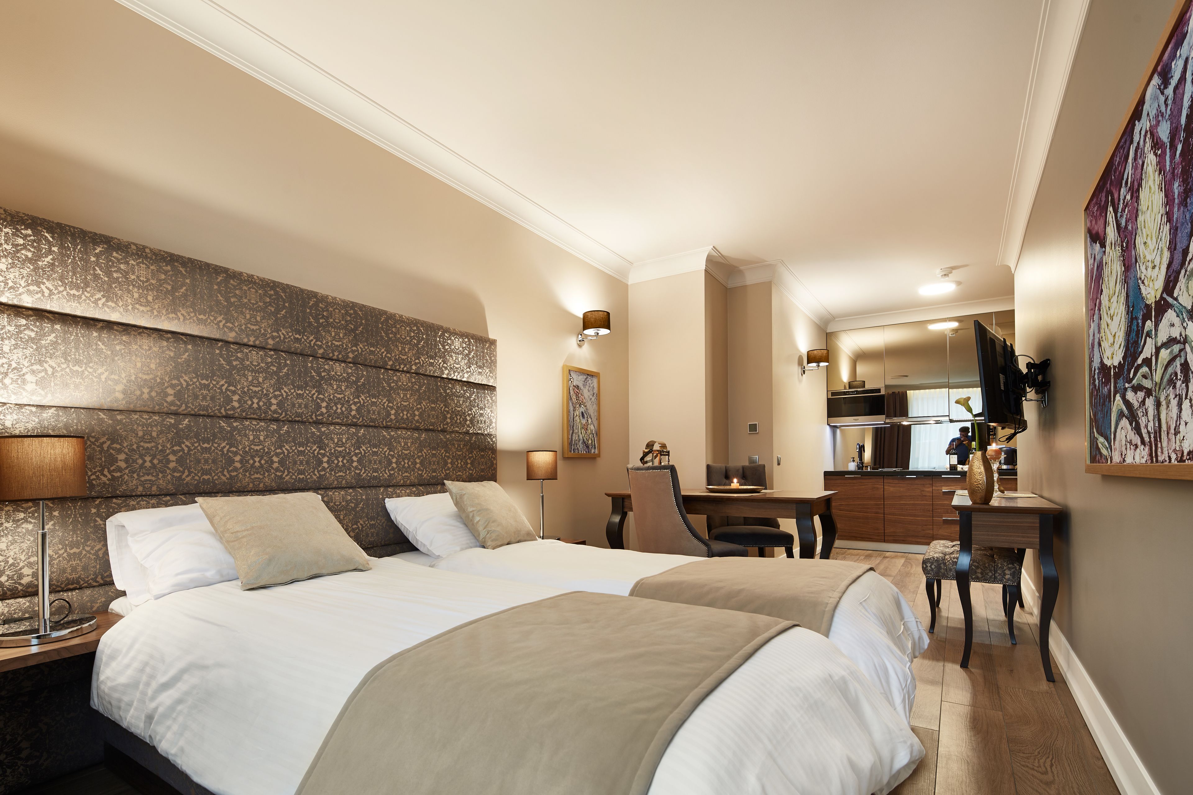 Een hotelkamer met twee bedden, een bureau, een stoel, een lamp en een schilderij aan de muur.