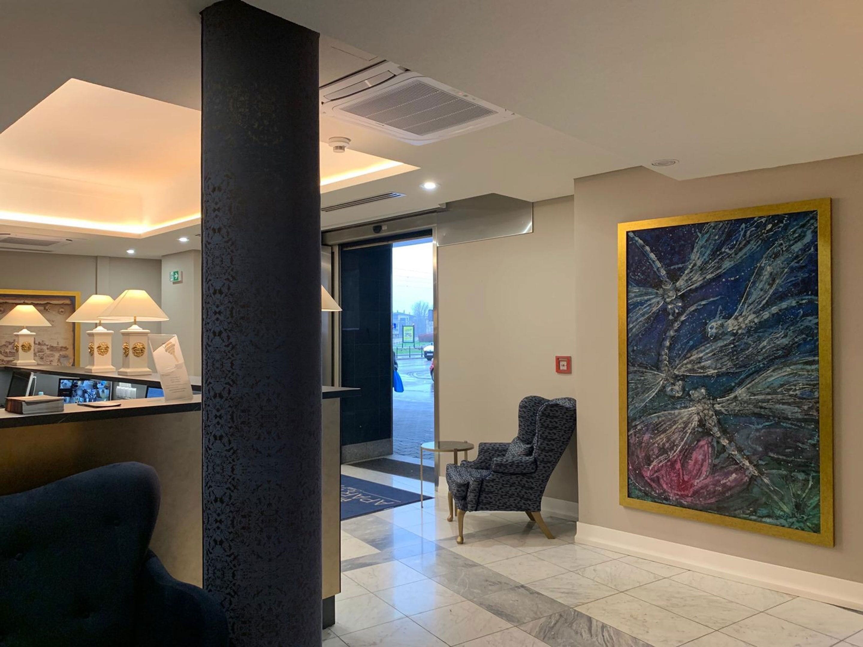 Un hall de hotel con una mesa de recepción, un cuadro abstracto de gran tamaño, un sillón estampado y vistas a la calle.
