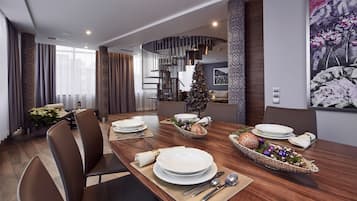 A modern dining area with a wooden table set for a meal, a Christmas tree, and a staircase leading to an upper level.