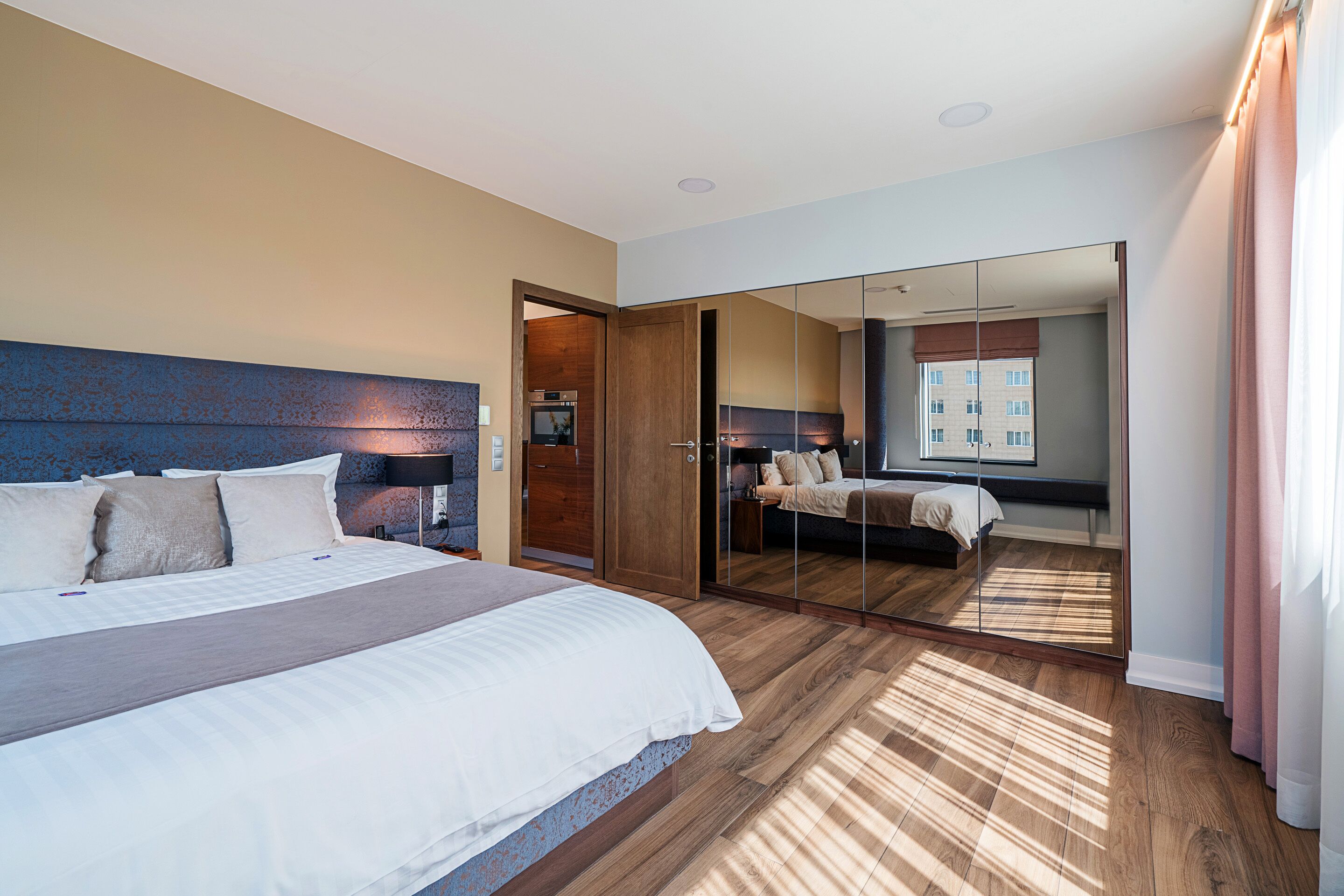 A modern hotel room with a large bed, a wardrobe, and a mirrored closet.