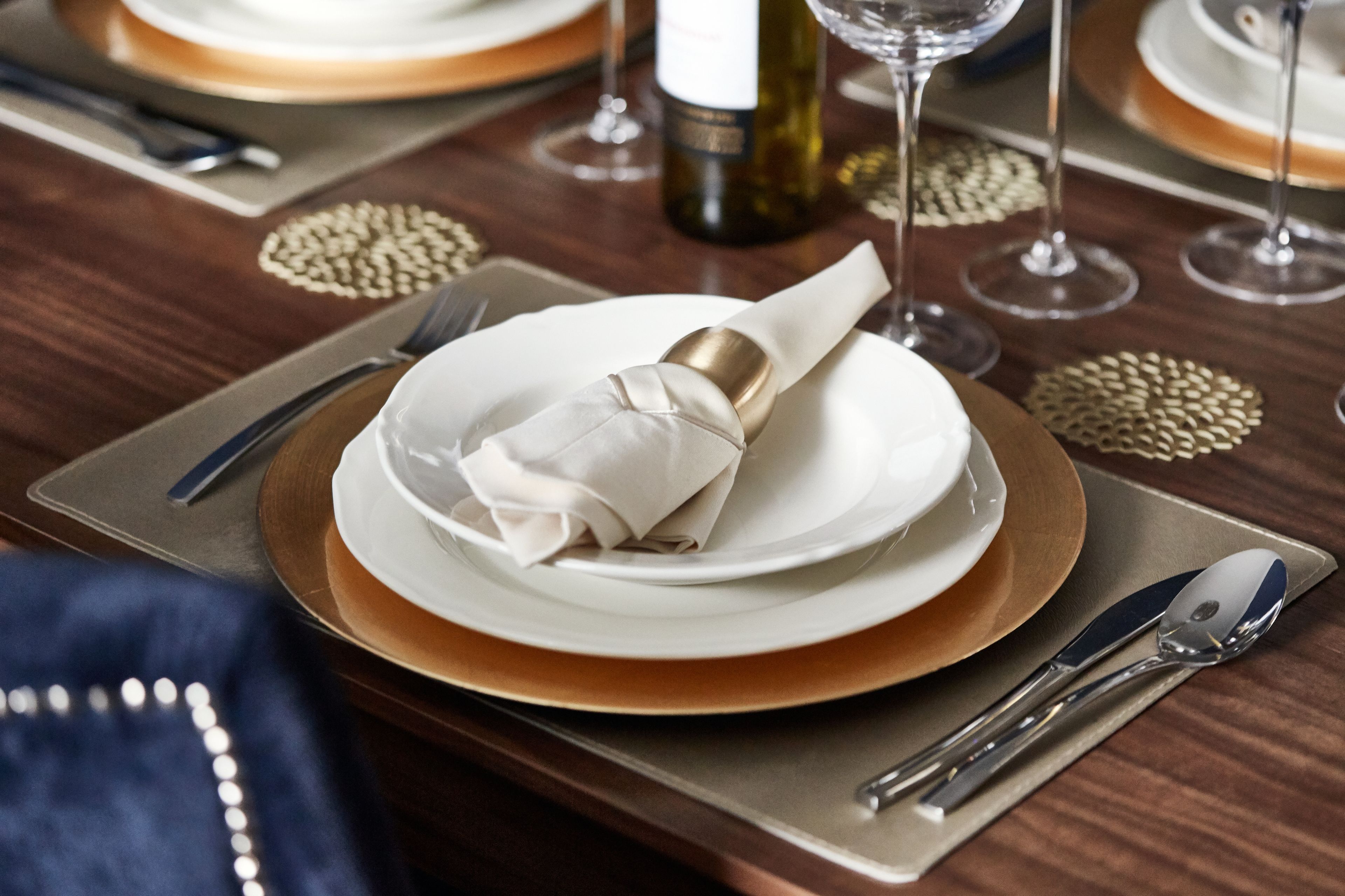 Une table dressée avec des assiettes, une serviette pliée, une bouteille de vin et des couverts.