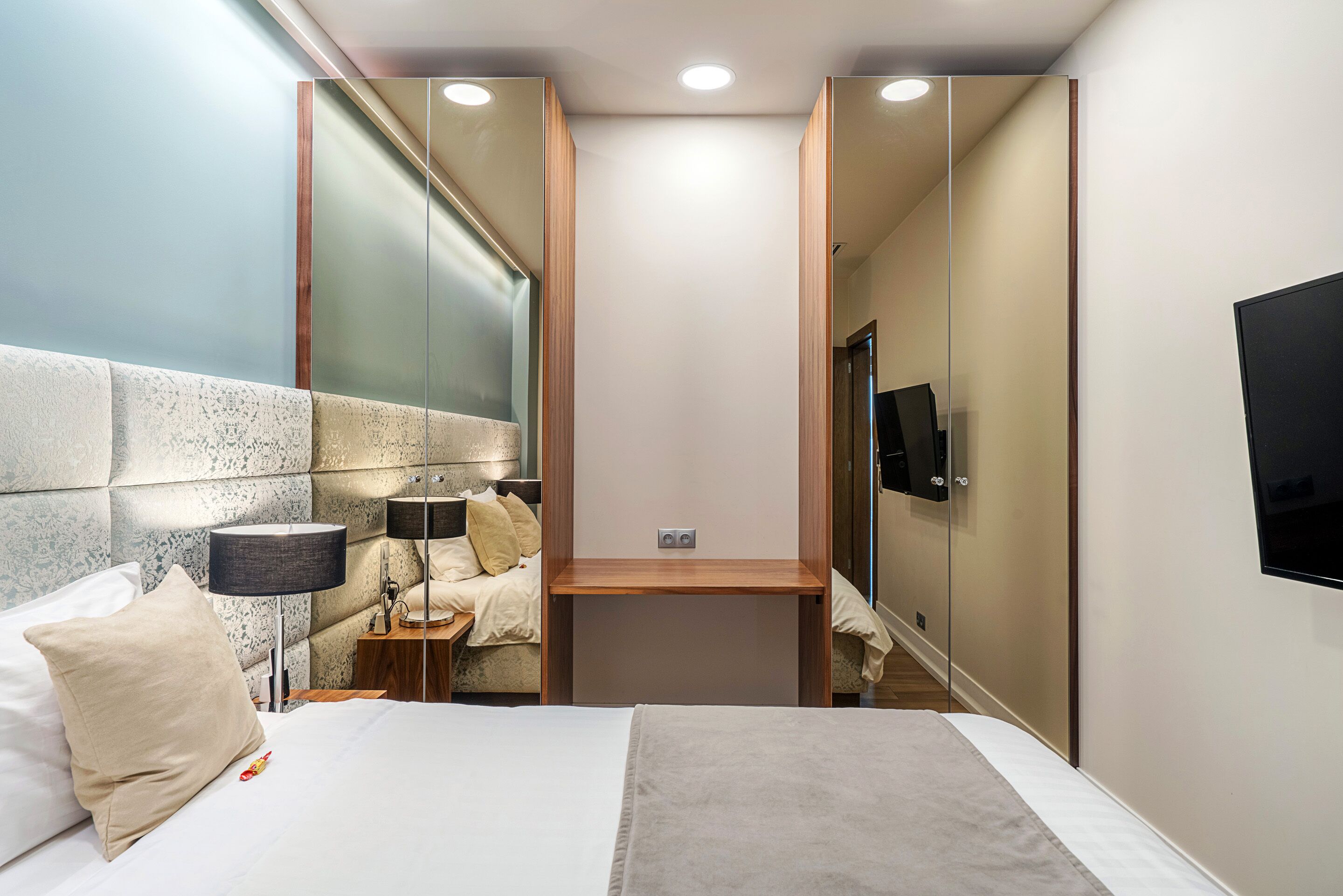 Una habitación de hotel moderna con una cama, mesita de noche, lámpara y un televisor montado en la pared.