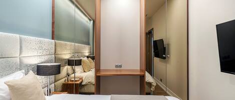 Una habitación de hotel moderna con una cama, mesita de noche, lámpara y un televisor montado en la pared.
