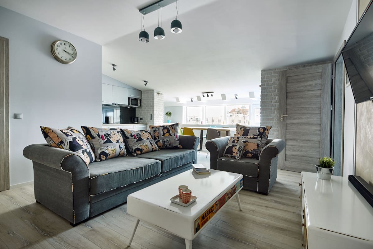 A modern living room with a grey sofa set, a white coffee table, and a kitchen in the background.