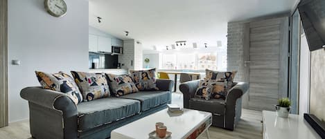 A modern living room with a grey sofa set, a white coffee table, and a kitchen in the background.