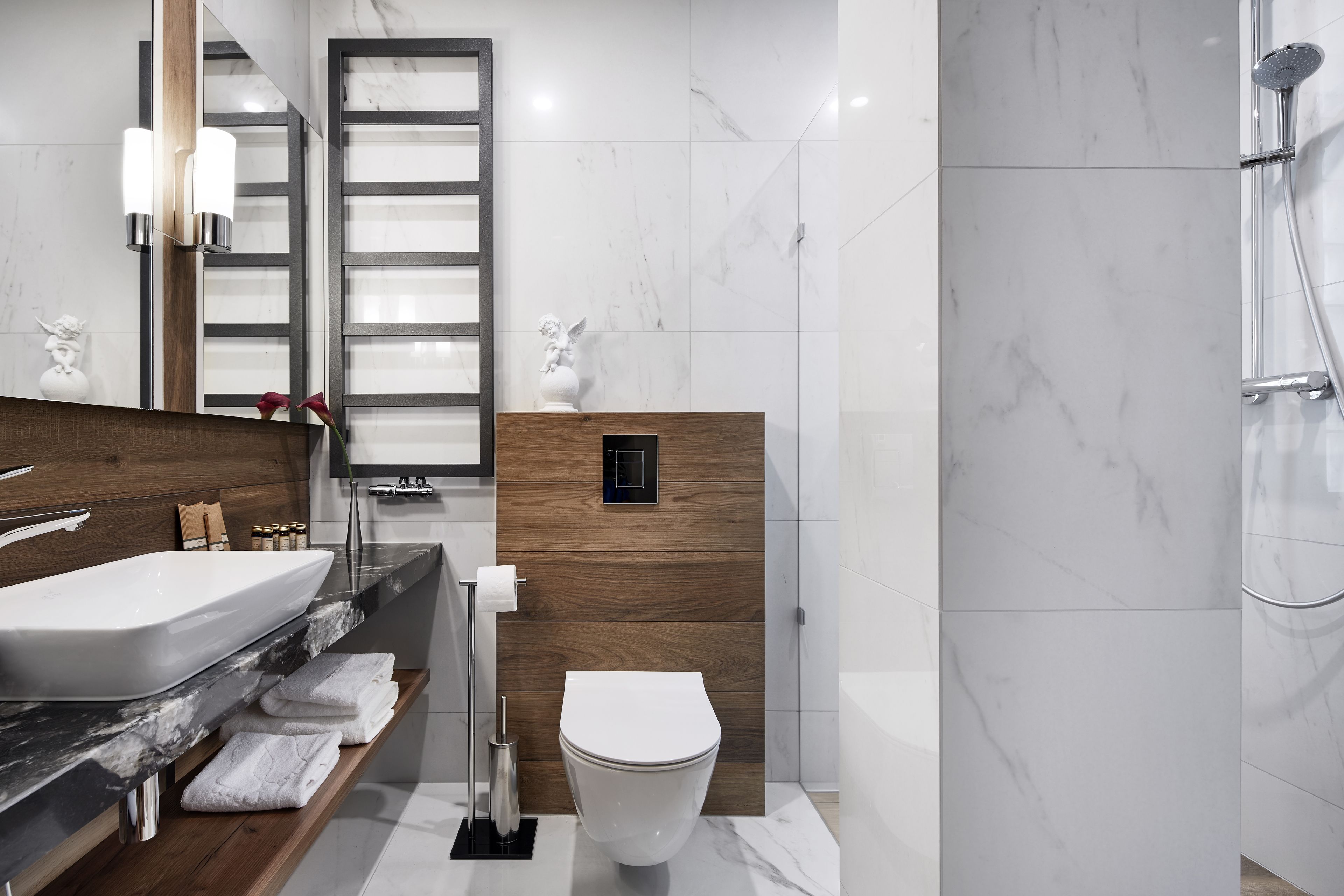 A modern bathroom with a large sink, wooden vanity, white toilet, and a shower area.