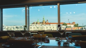 A dining table with wine glasses and a view of a cityscape through large windows. - Aparthotel Best Views Luxury (Kraków)