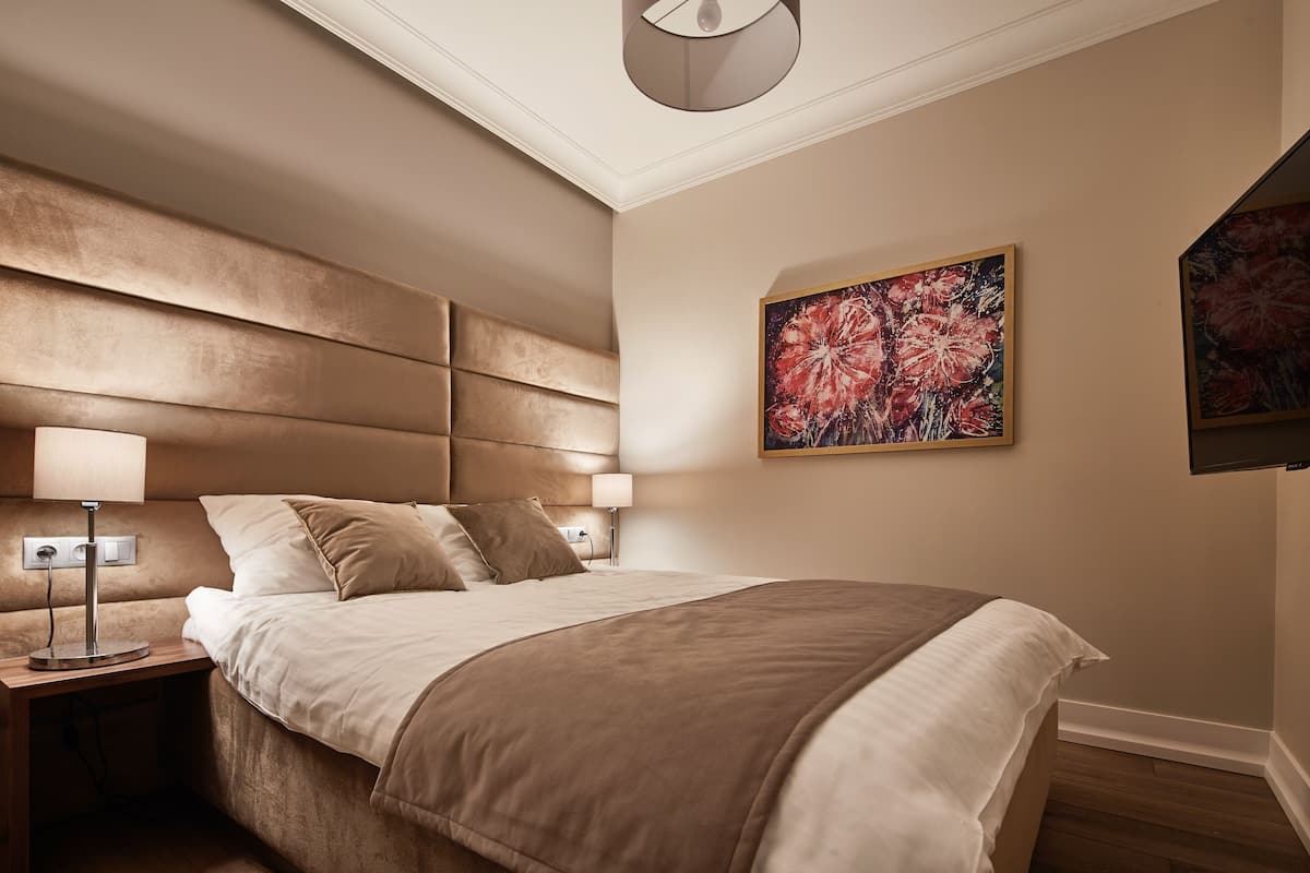 A modern hotel room with a large bed, a nightstand with a lamp, and a painting on the wall.