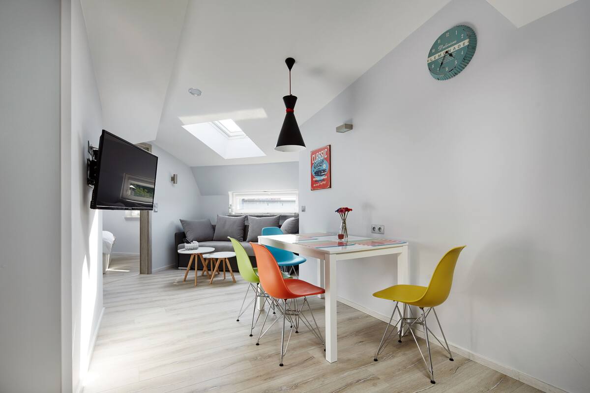 A modern kitchen with a dining area, a TV mounted on the wall, and a skylight.