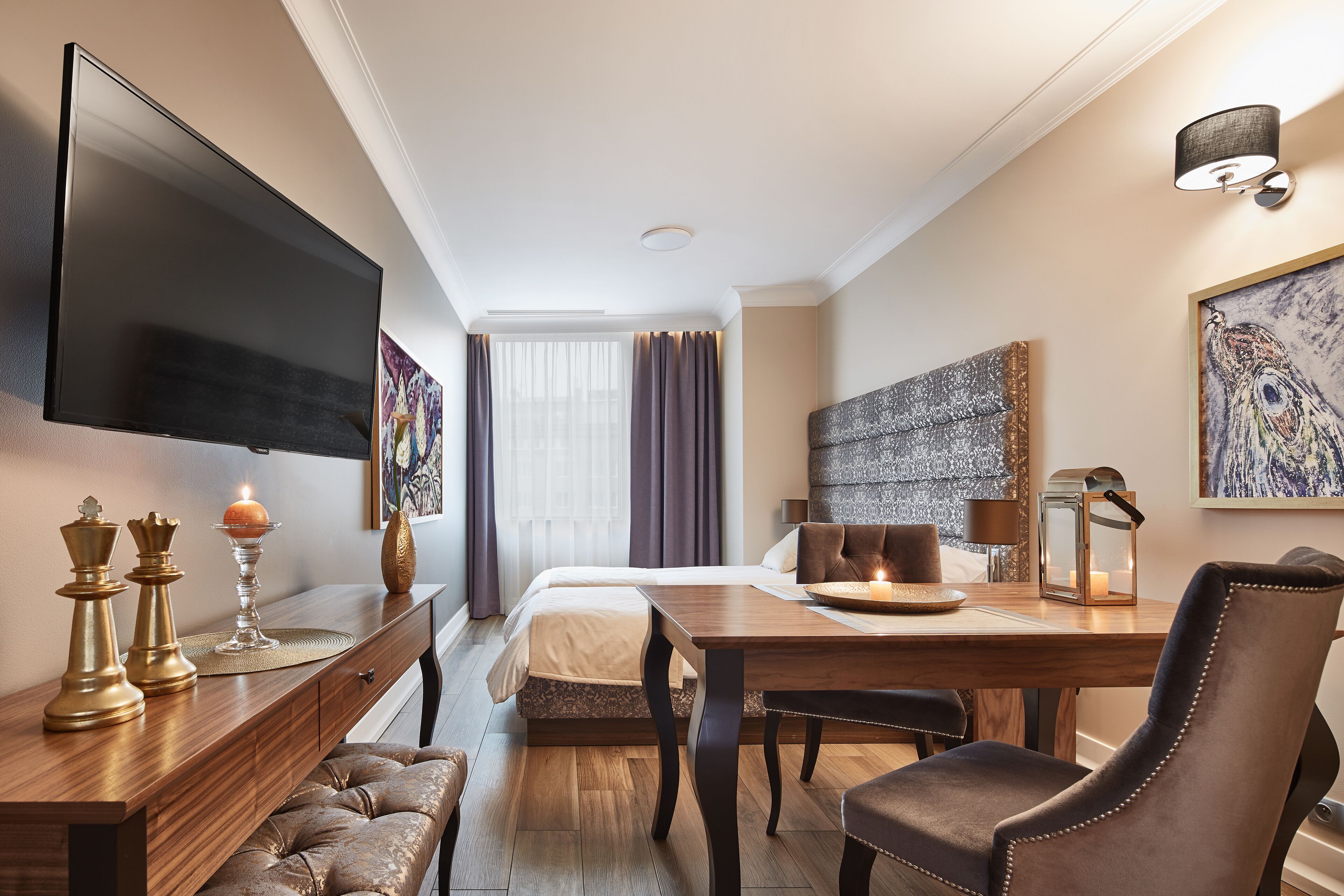 Una habitación de hotel con una cama, un escritorio de madera, un televisor y obras de arte en las paredes.