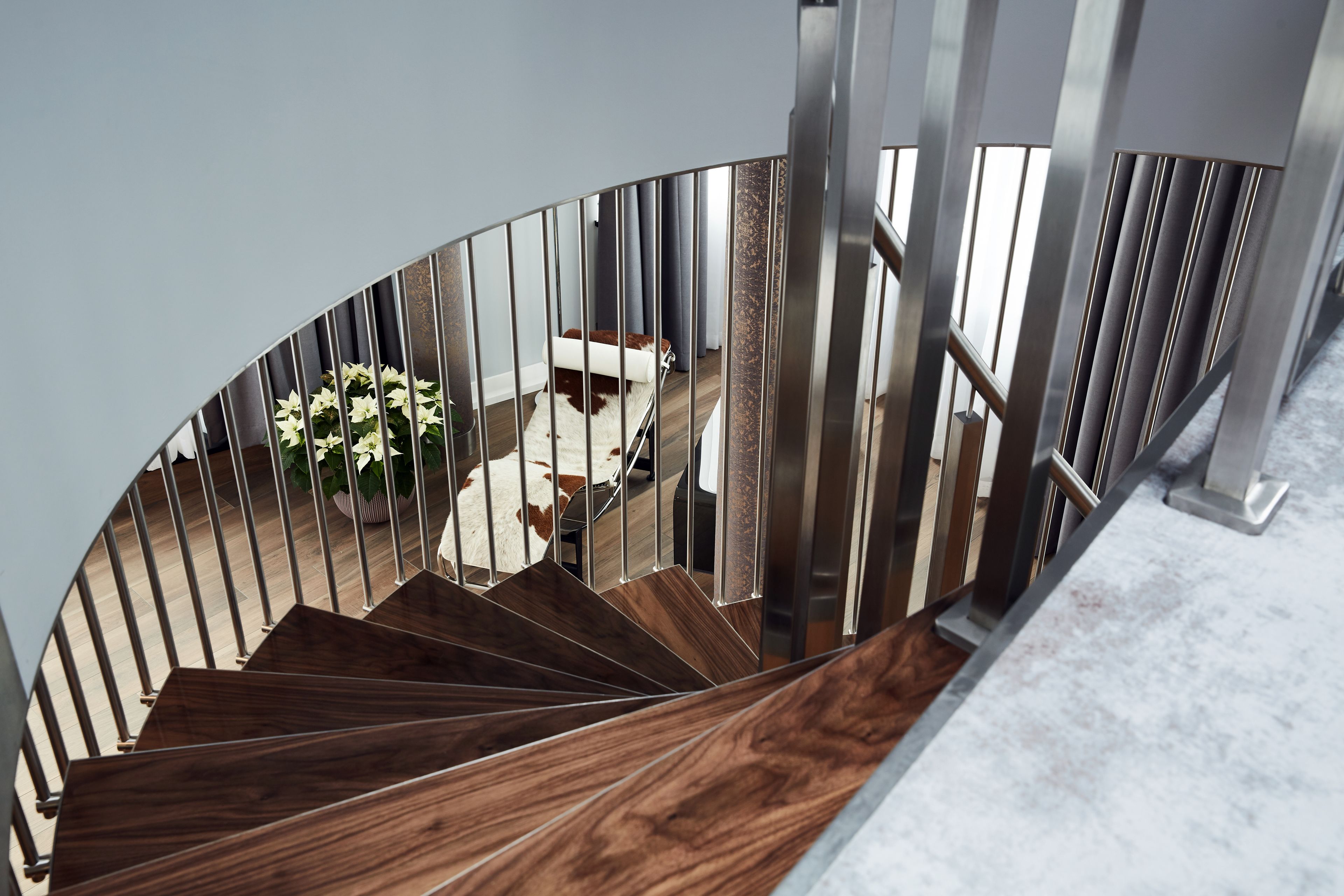 Un escalier en colimaçon avec des marches en bois et des rampes en métal, menant à une pièce où se trouvent un canapé blanc et une plante en pot.