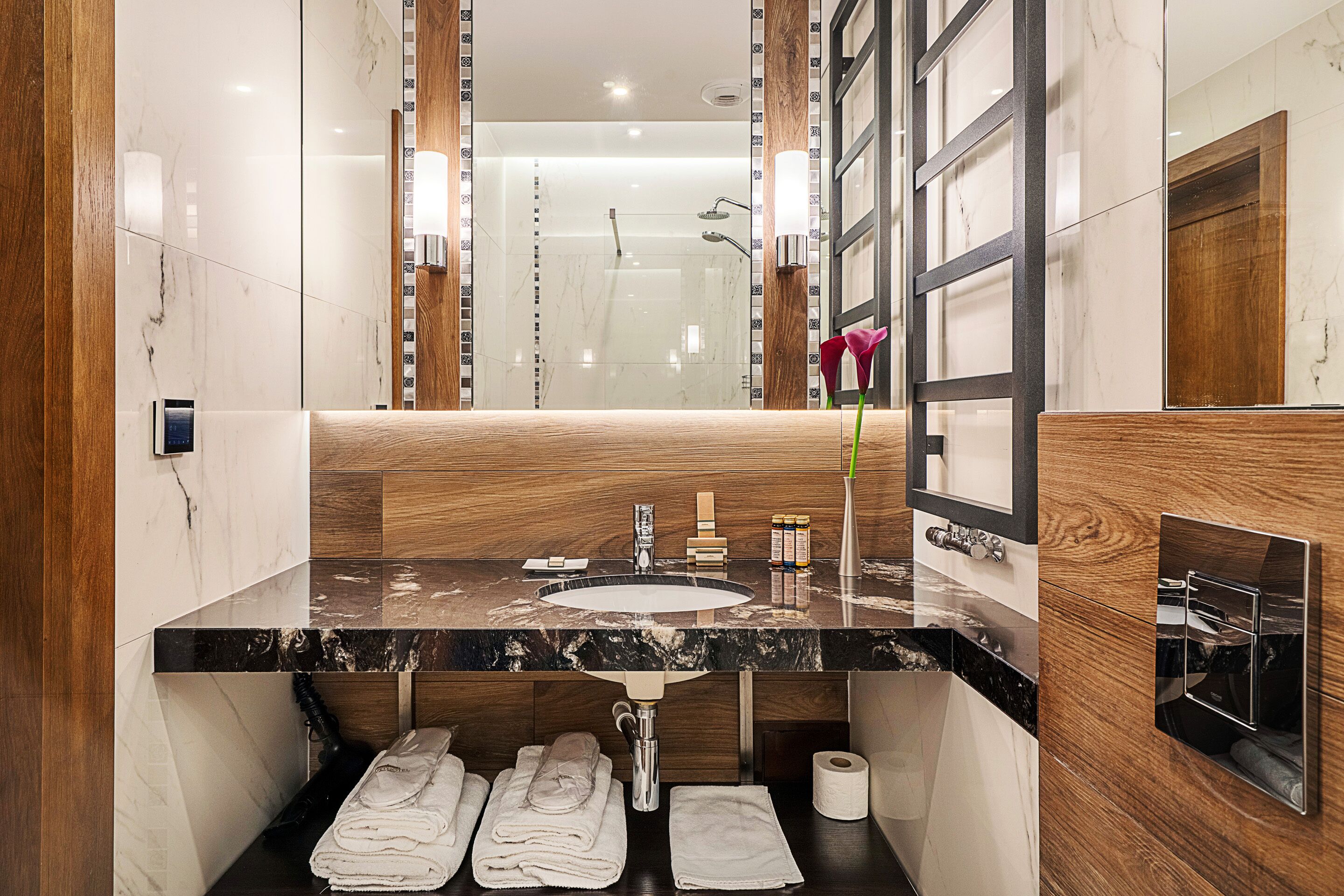 A modern bathroom with a marble sink, wooden vanity, and a large mirror.