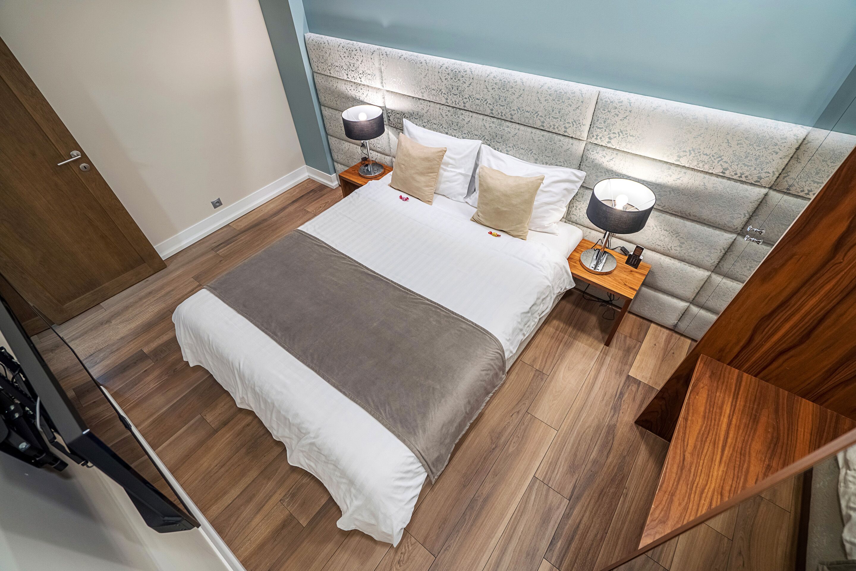 A modern bedroom with a large bed, two bedside tables with lamps, and a wooden floor.