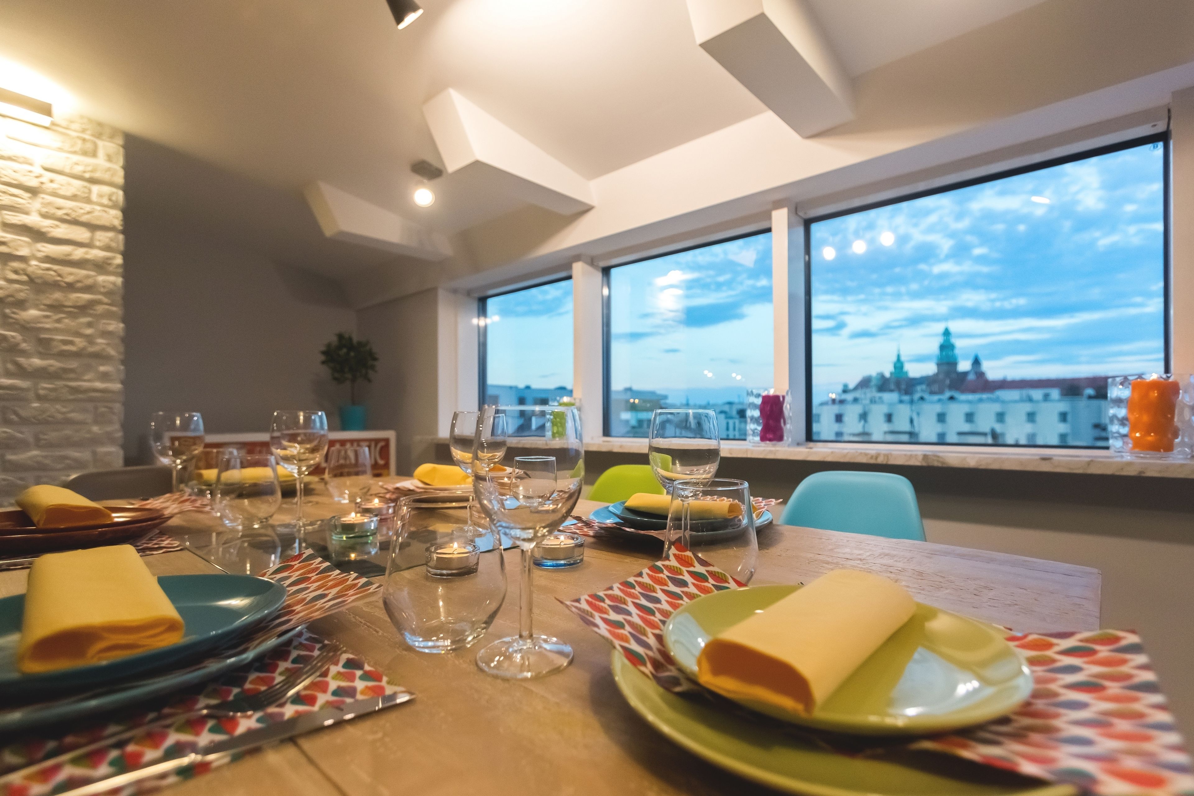 Une table à manger dressée avec des assiettes, des couverts et des verres, offrant une vue sur le paysage urbain à travers de grandes fenêtres.
