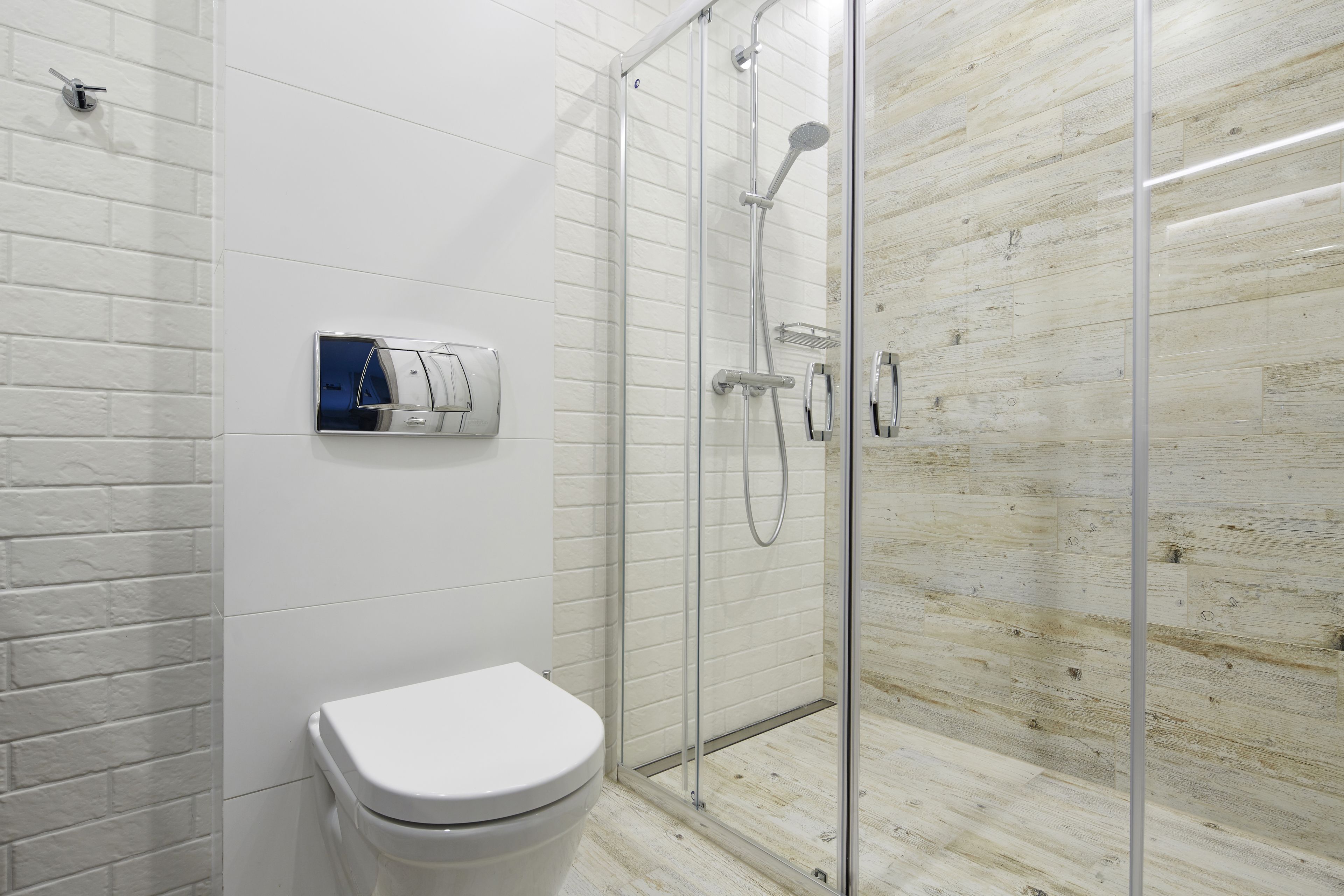 A modern bathroom with a glass-enclosed shower, a white toilet, and a wall-mounted control panel.