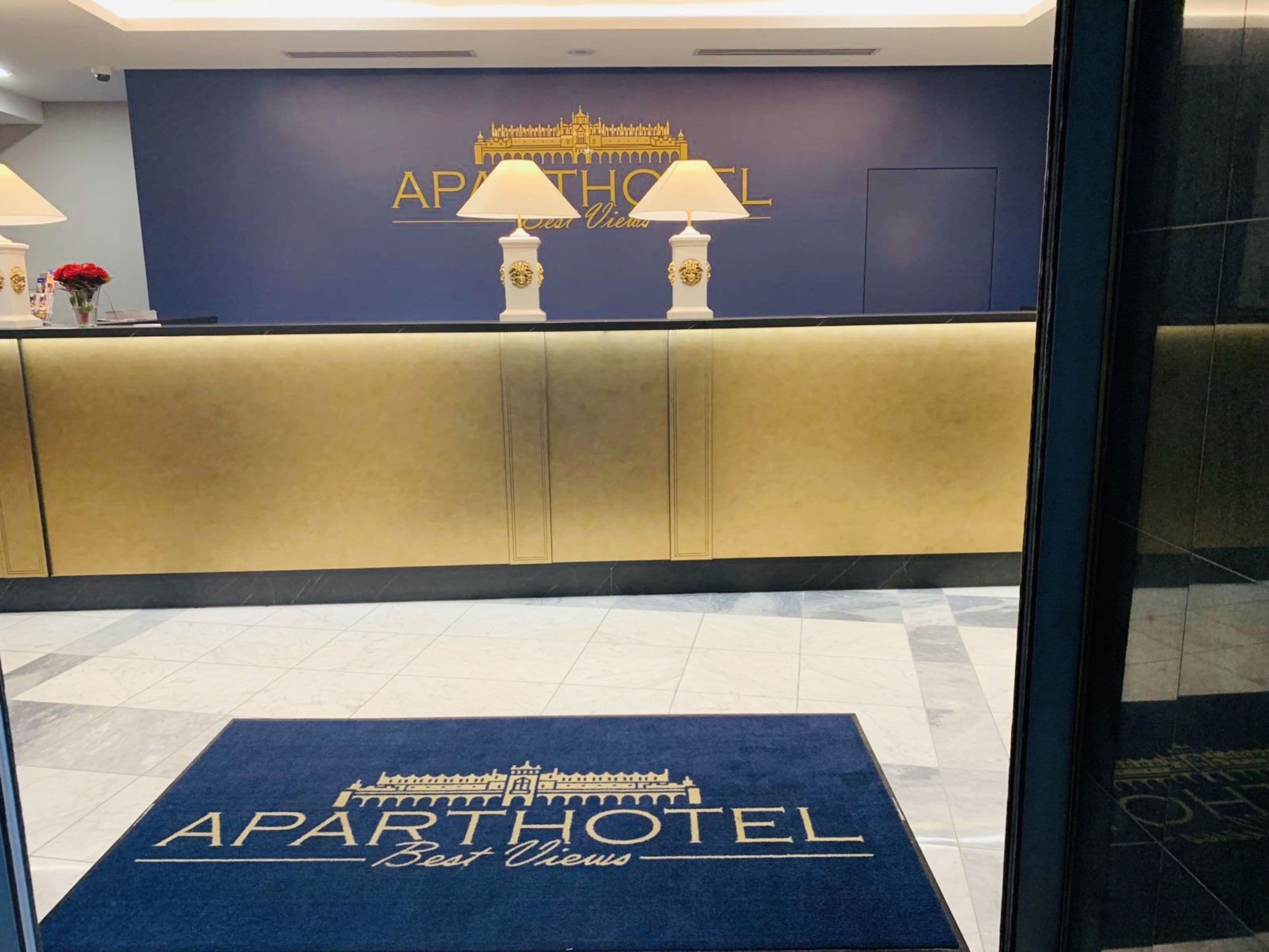A reception desk with a blue backdrop displaying the name 'APARTHOTEL' and 'Best Views'.