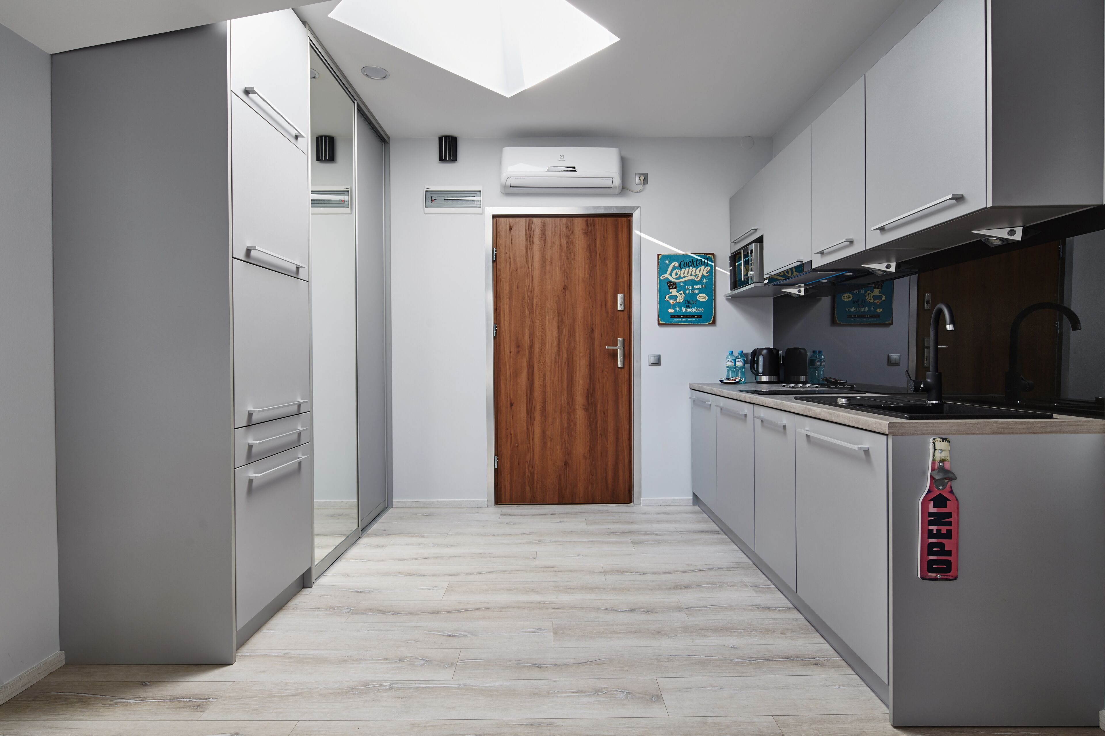 Una cocina moderna con armarios grises, una puerta de madera y un cartel abierto en el refrigerador.