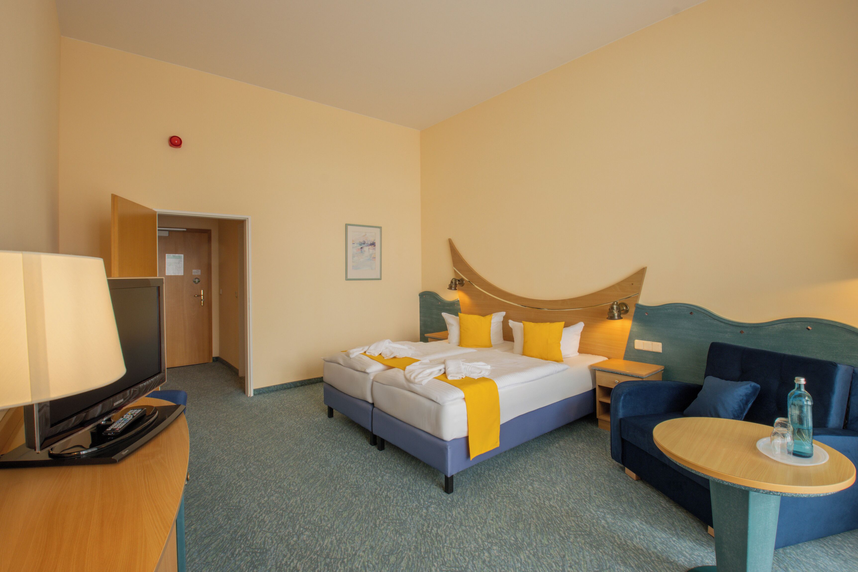 A hotel room with a bed, a desk with a lamp, a chair, and a small table.