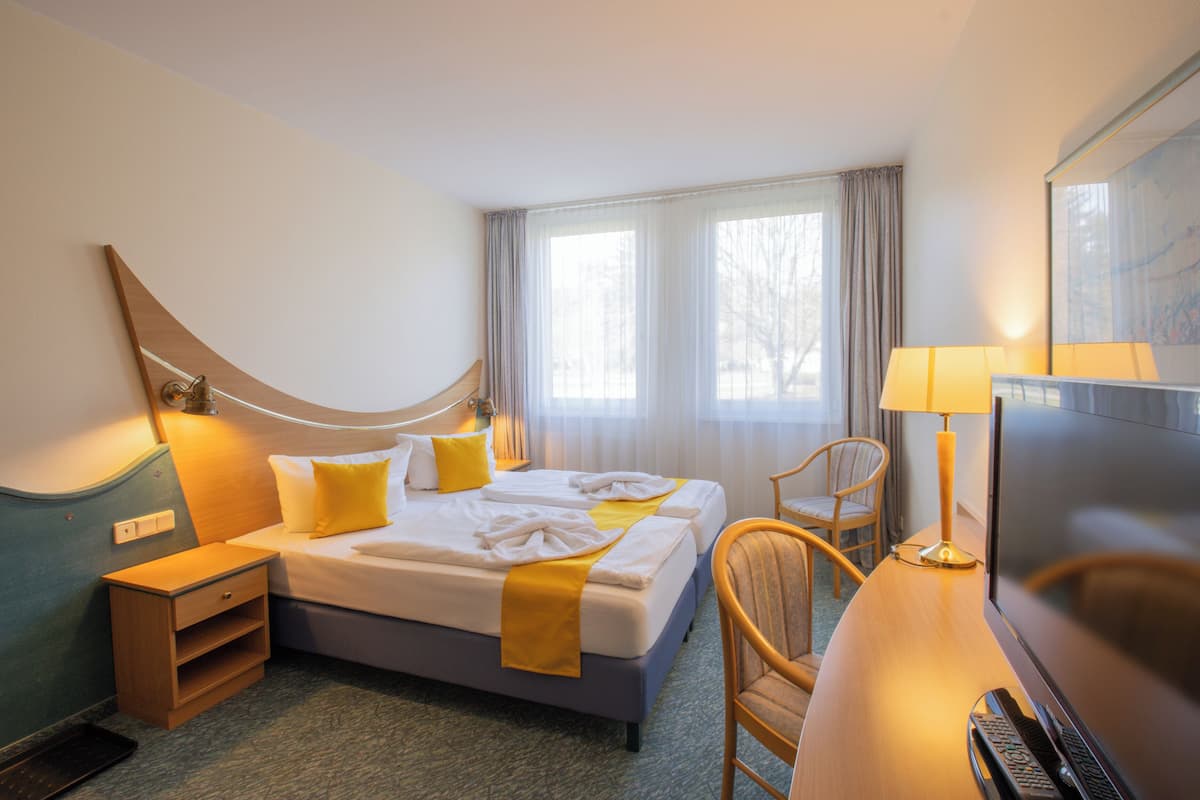 A hotel room with two beds, a desk with a TV, a chair, a lamp, and a window with curtains.