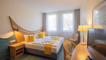 A hotel room with two beds, a desk with a TV, a chair, a lamp, and a window with curtains.
