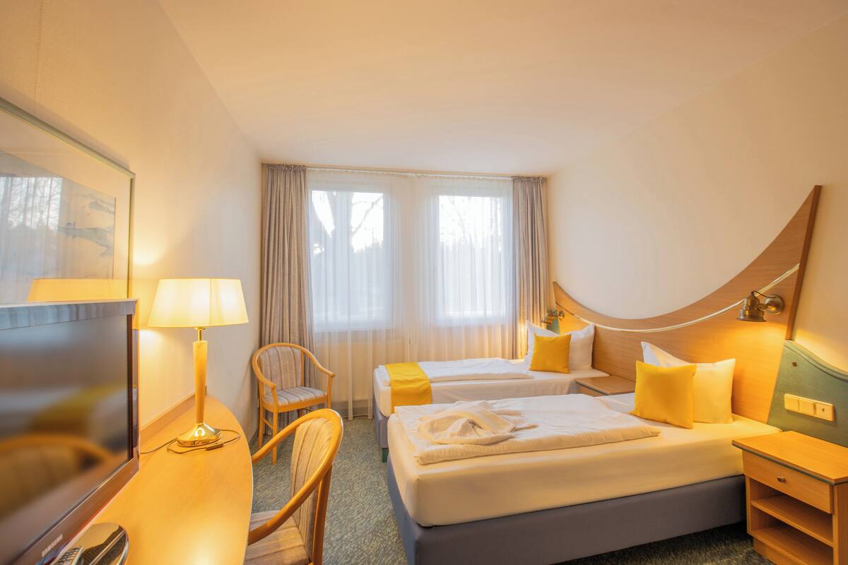 A hotel room with two beds, a desk, a chair, a TV, and a window with curtains.