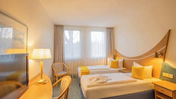 A hotel room with two beds, a desk, a chair, a TV, and a window with curtains.