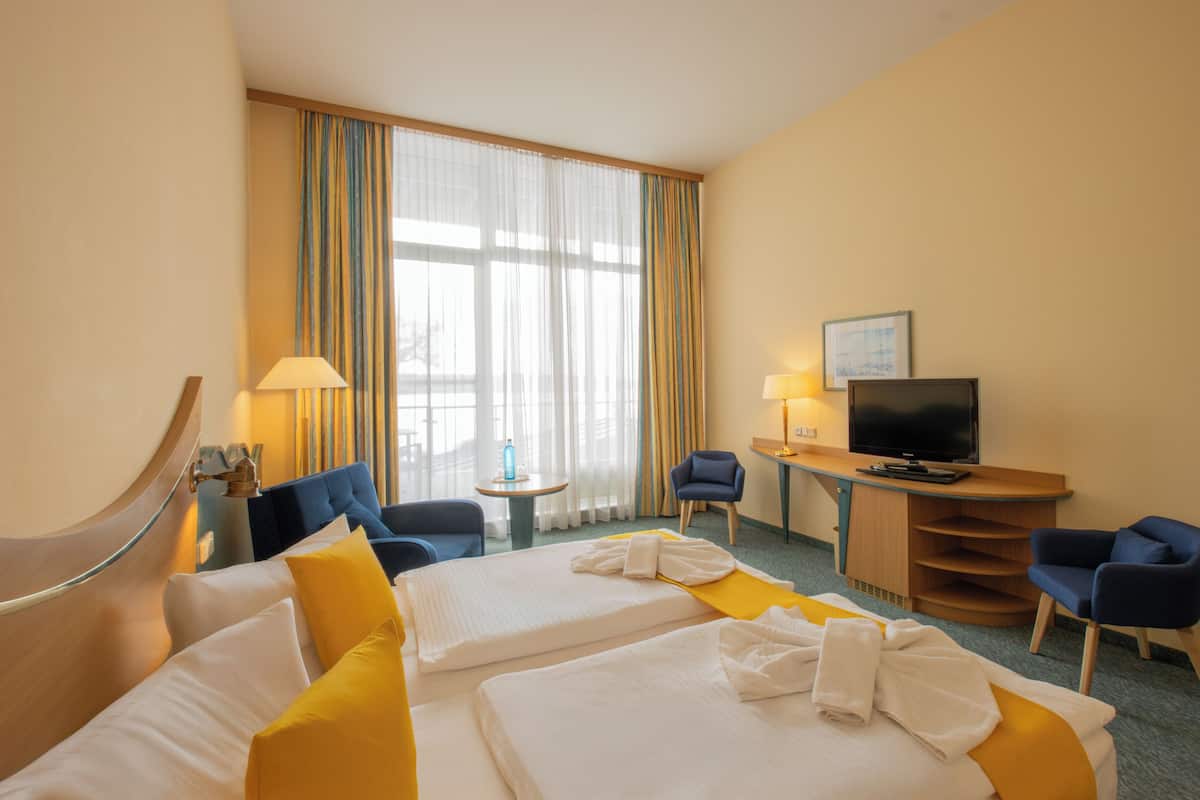 A hotel room with two beds, a desk with a television, a chair, and a small table with a bottle.