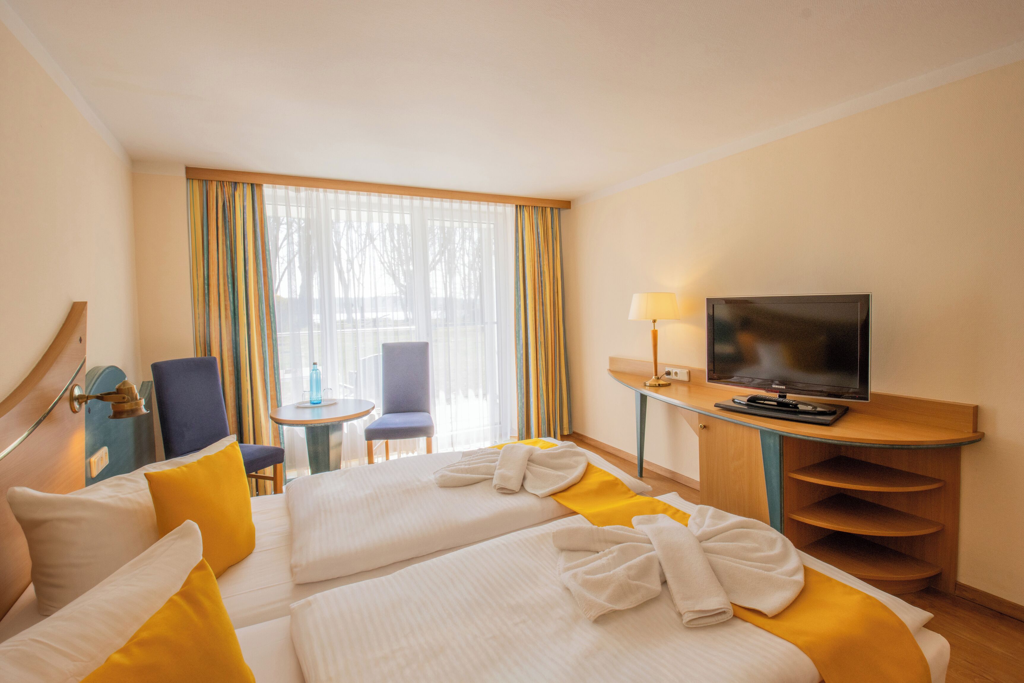 Une chambre d’hôtel avec deux lits, une télévision, un bureau, une chaise et une fenêtre avec des rideaux.