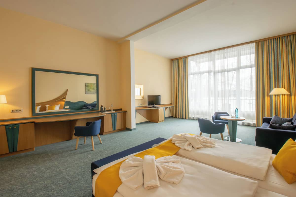 A hotel room with two beds, a desk, a TV, a small table, and a seating area with chairs.