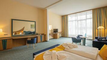 Habitación de hotel con dos camas, un escritorio, televisión, una mesita y un área de descanso con sillas.