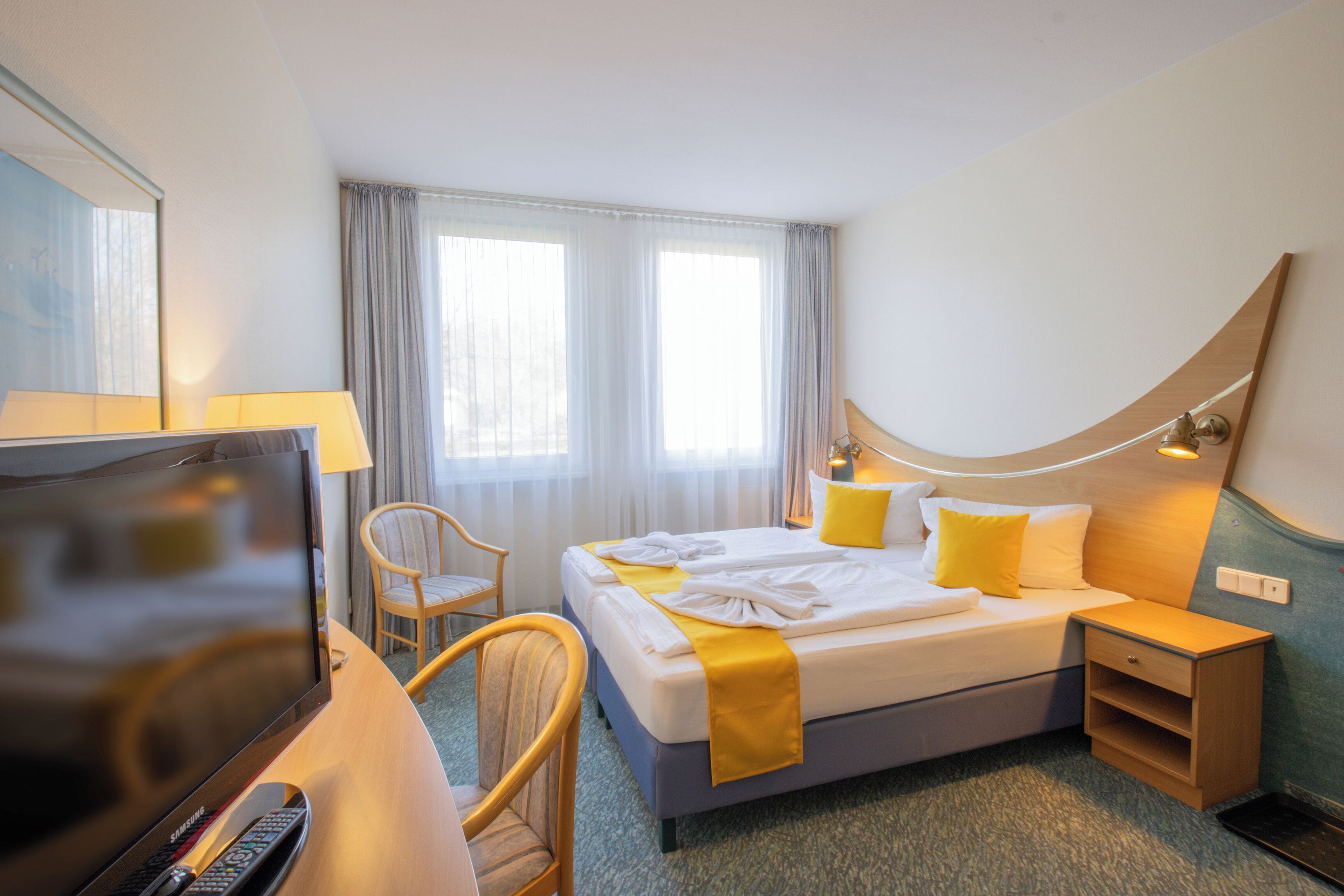 Et hotelværelse med seng, fjernsyn, skrivebord med lampe, stol og et natbord.