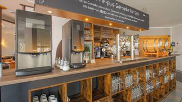 A coffee bar with espresso machines, a coffee press, and shelves with glassware and bottles.
