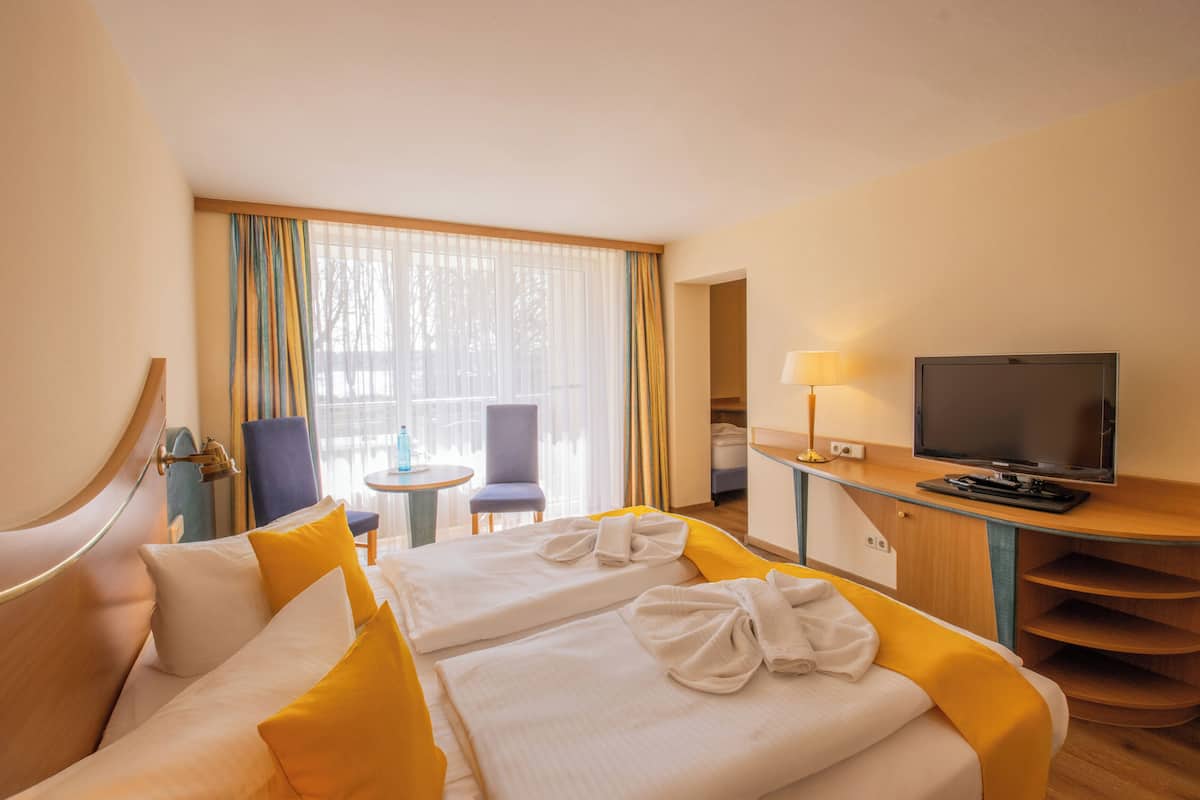 A hotel room with two beds, a TV, a desk, a chair, and a window with curtains.