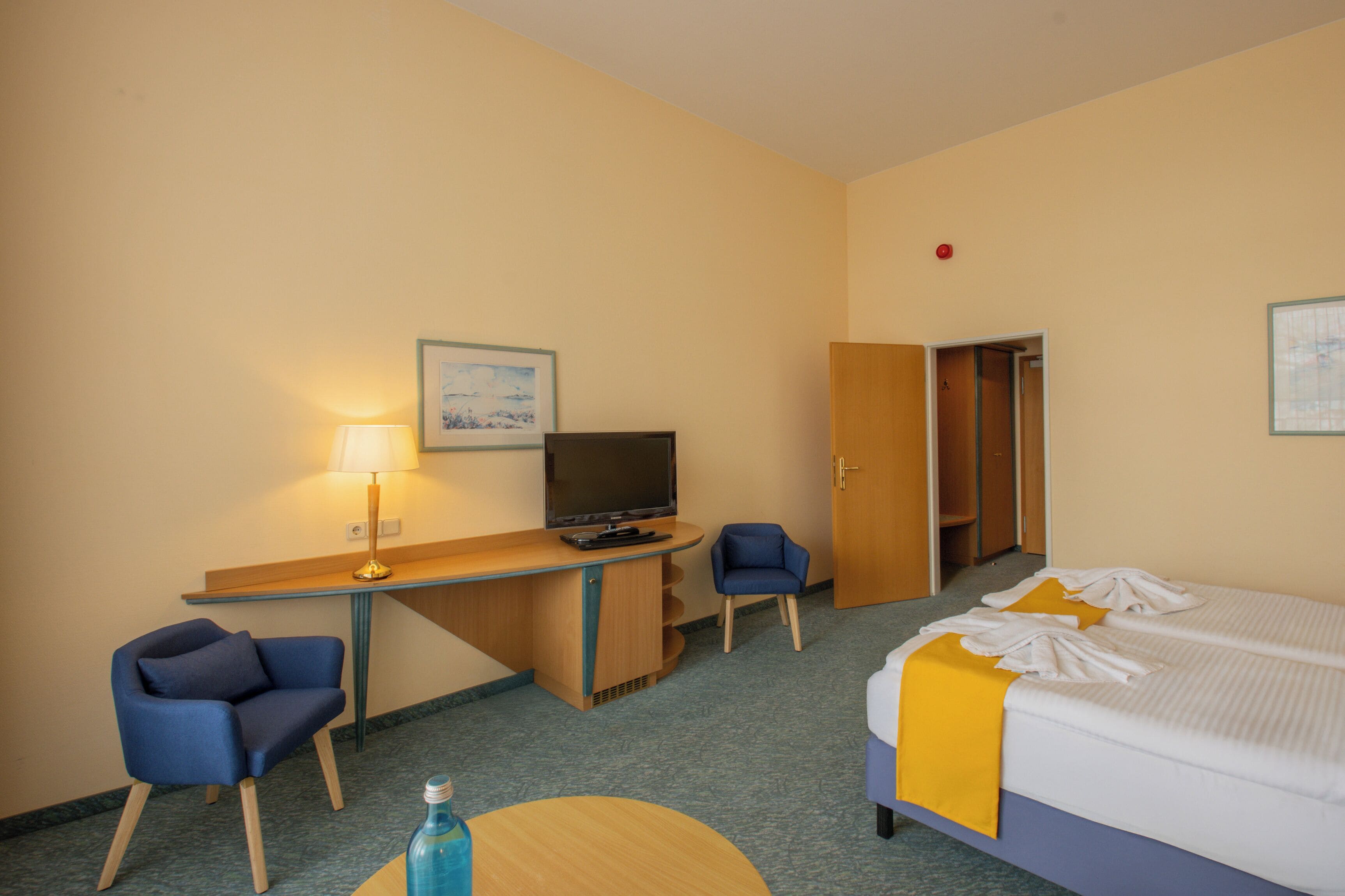 Une chambre d’hôtel comprenant un lit, un bureau avec un ordinateur et une télévision, une chaise et une petite table.